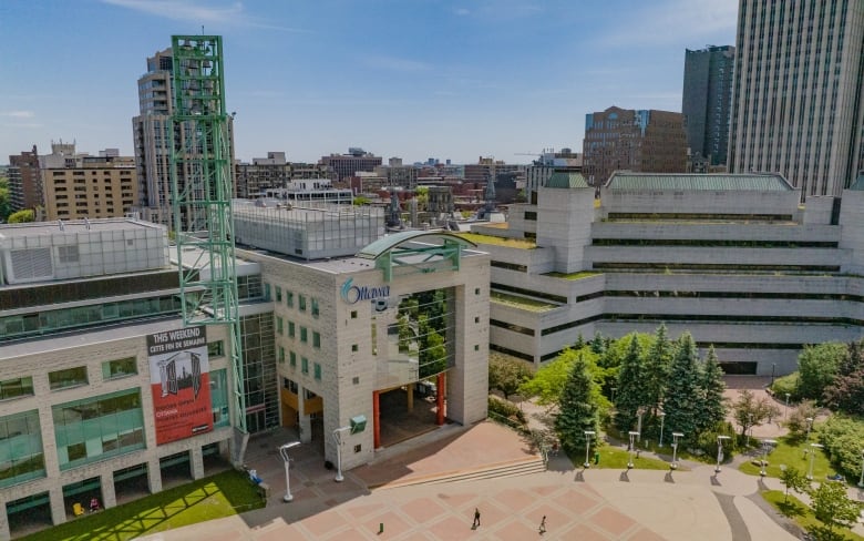 A photo taken with a drone of Ottawa City Hall downtown. The sky is sunny and the trees are green. The courtyard is relatively empty.